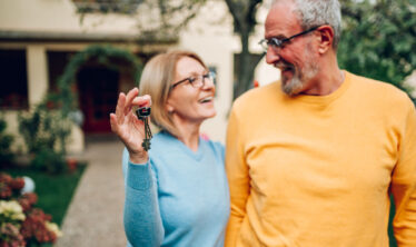 casal-idosos-segurando-chaves-em-pe-em-frente-de-casa